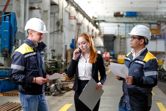 Young successful engineers are discussing the technical documentation. Engineers at the factory in work clothes.