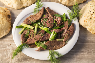 lamb liver food with green vegetables in the plate and local bread on the wooden table for restaurant and kitchen concept.