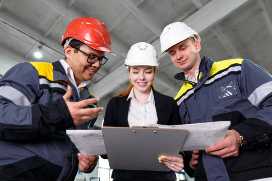 Young engineers and workers discuss technical documentation. Work in a modern factory. Girl engineer explains the work plan.