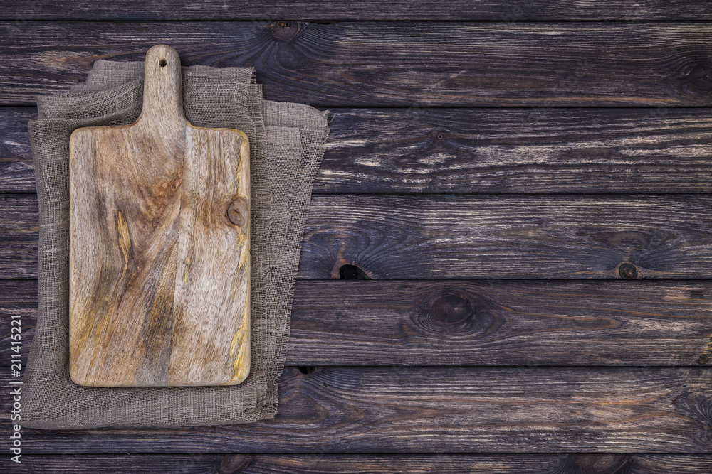 Wall mural Old cutting board on dark wooden table. Top view. Copy space