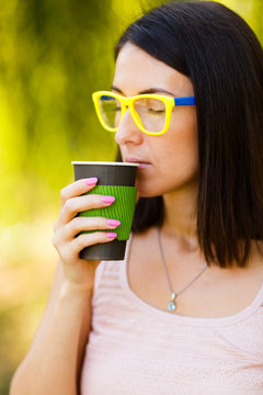hipster girl in yellow glasses is holding coffee in a paper cup