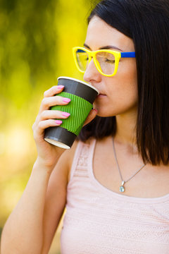 hipster girl in yellow glasses is holding coffee in a paper cup