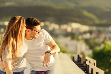 Fototapeta na wymiar Attractive couple on balcony watching the city on sunset. Young and careless having fun concept.