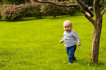 smiling little boy walking on green grass in jeans and shirt