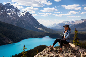 Adventurous girl sitting on the edge of a cliff overlooking the beautiful Canadian Rockies and Peyto Lake. Taken in Banff National Park, Alberta, Canada.