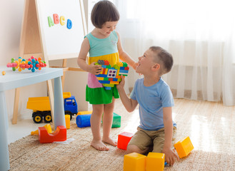 A boy and a girl are holding a heart made of plastic blocks. Brother and sister have fun playing...