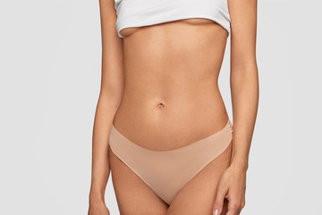 Fototapeta na wymiar Perfect slim body, elastic belly and healthy skin. Sporty female in white top and beige pants, shows fit figure after sport training. Advertisement of lingerie for women. Motivation concept.