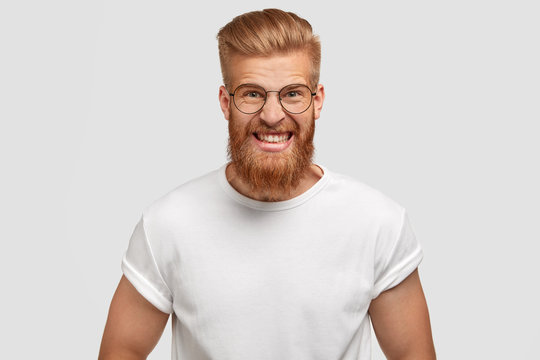 Negative facial expressions concept. Depressed angry irritated male model with ginger thick beard, strong muscular body, clenches teeth in annoyance, being fed up of everyday life, has problems