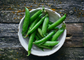 Healthy organic fresh green peas in bowl on wooden table top view 
