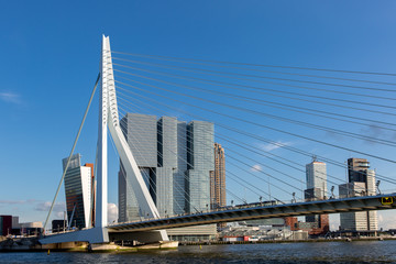 Cityscape of Rotterdam at sunset with the Erasmus bridge in the foreground and high rise buildings of the financial district in the Dutch city in the background against a clear blue sky