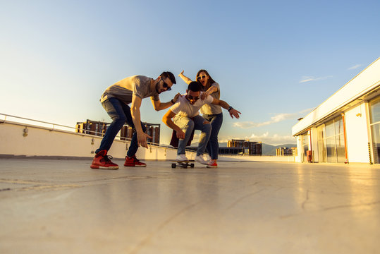 Three friends amuse on rooftop with skateboard. Young and careless friends having fun concept.