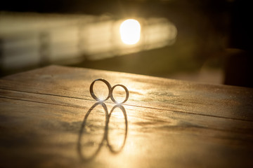 Romantic scene with wedding rings on wooden table illuminated by sunset light
