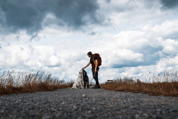 Young woman feeds two dogs on a walk in front of a dramatic sky