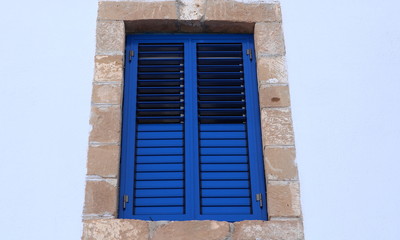 Exterior view of a blue window with closed shutters in brick frame. 