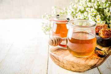 Organic floral honey, in jars, with pollen and honey combs, on a white wooden table, with wildflowers, copy space
