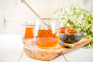 Organic floral honey, in jars, with pollen and honey combs, on a white wooden table, with wildflowers, copy space