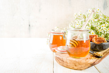 Organic floral honey, in jars, with pollen and honey combs, on a white wooden table, with wildflowers, copy space