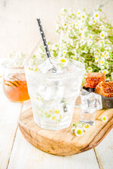 Organic diet detox summer beverage, infused water drink with camomile and honey, on white wooden table, with chamomile flowers and honey in a jar. Copy space