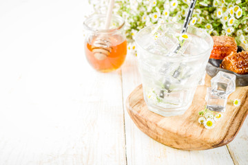Organic diet detox summer beverage, infused water drink with camomile and honey, on white wooden table, with chamomile flowers and honey in a jar. Copy space