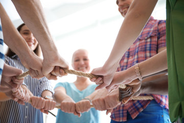People holding rope together on light background, closeup of hands. Unity concept