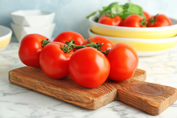 Wooden board with fresh ripe tomatoes on table