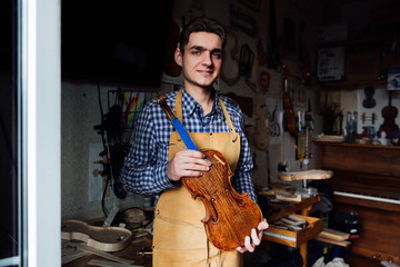 portrait of a young luthier with a handcrafted violin in his workshop with the tools.
