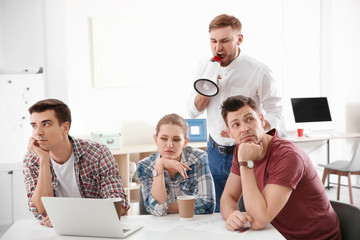 Angry boss with megaphone screaming at employees in office