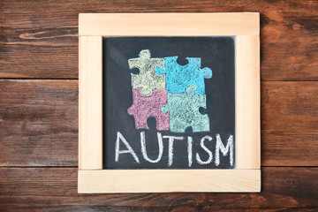 Chalkboard with word AUTISM and drawn puzzle pieces on wooden background