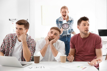 Angry boss with megaphone screaming at employees in office
