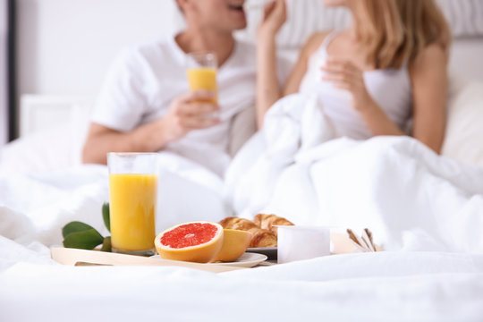 Tray with healthy breakfast on bed of young happy couple