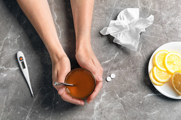 Woman holding glass with hot tea for cold on table, top view