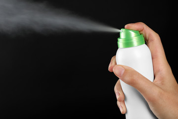 Young woman spraying deodorant on black background
