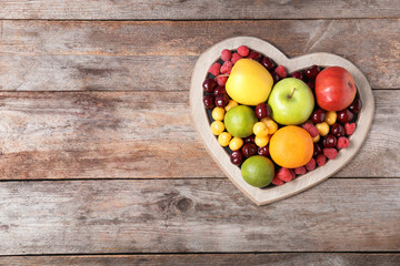 Heart shaped plate with fresh fruits on wooden table, top view. Cardiac diet