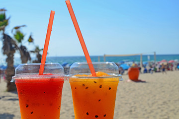 Two bright fruit cocktails with ice in glasses with tubes..Cool drinks on the beach against the backdrop of palm trees and the sea...