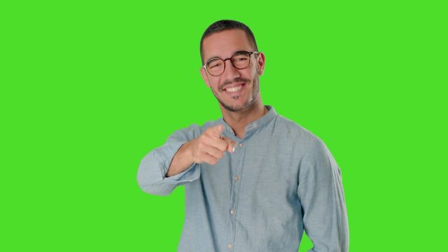 Happy young man on chroma screen pointing at you