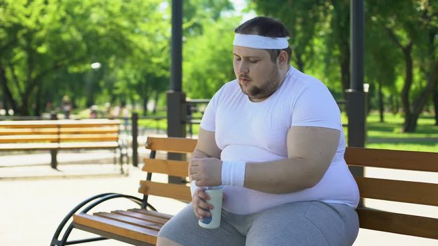 Fat man breathing heavily and drinking water after intense workouts in park