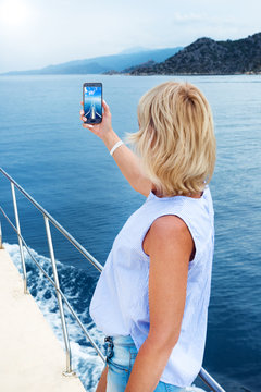 Beautiful woman taking photo on sailboat using smart phone technology for social media in ocean on luxury lifestyle adventure travel vacation. travel and active lifestyle concept