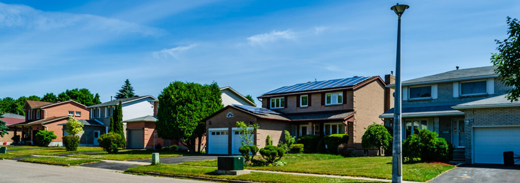 Panorama of a row of residential houses along a street, one with solar panels on the roof