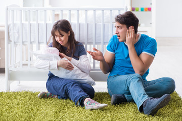 Young parents with their newborn baby sitting on the carpet 