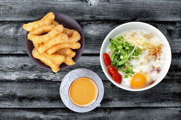 Rice porridge with mined pork served with a cup of coffee and  Patongko (deep-fried dough stick) on old black wood.