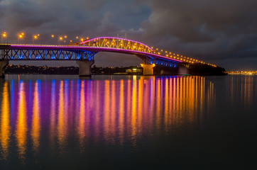 Auckland harbour bridge at night lit up in bright colours.
