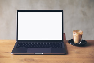 Fototapeta premium Mockup image of laptop with blank white desktop screen and coffee cup on wooden table with concrete wall background