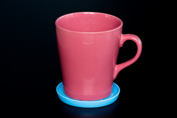 Red cup in blue plate on the black background.