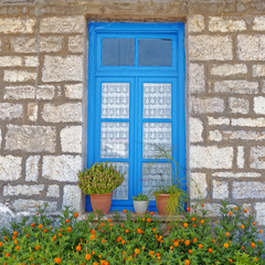 Fototapeta na wymiar Greece, stone wall house blue window and marigold flowers
