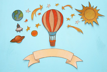 Hot air balloon, space elements shapes cut from paper and painted over wooden blue background.