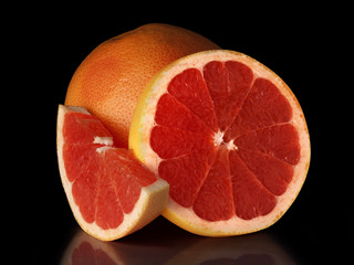 A large ripe grapefruit with cut slices on a black background