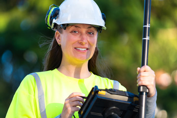 Woman in reflective clothing smiling while using GPS land surveying tool with screen