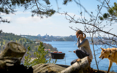 Woman grilling hamburger on charcoal barbecue in front of Stockholm skyline