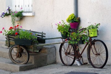 Fototapeta na wymiar Old bicycle and cart with flowers leaning against house wall