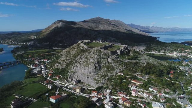 Beautiful drone flight towards historic castle built on mountain overlooking Shkoder lake in Albania, Southeastern Europe